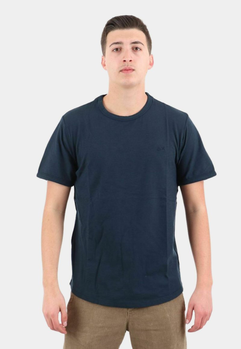 T-shirt in cotone blu navy con maniche corte, collo tondo e un logo discreto. Abbinato a pantaloni in velluto a coste color marrone chiaro.