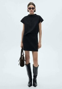 Black dress with a structured, short-sleeve top and fitted skirt. Paired with tall black boots and a brown shoulder bag. Smooth fabric texture.