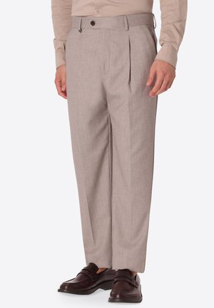 Pantaloni da uomo beige plissettati da cerimonia abbinati a mocassini in pelle marrone e camicia beige chiaro a maniche lunghe.