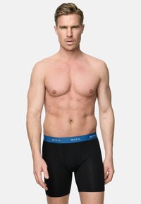 Svarta boxershorts med ett blått midjeband som har vit text. Tyget ser mjukt och elastiskt ut, vilket formar en åtsittande passform.