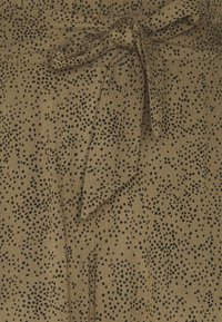 Brązowa tkanina z cętowanym czarnym wzorem w kropki, związaną wstążką i gładką teksturą. Zbliżenie na materiał odzieżowy.