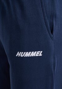 Close-up van marineblauwe stoffen broek met zijzak en wit "HUMMEL"-logo gedrukt vlak bij de zaknaad.