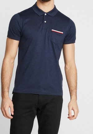 Granatowa koszulka polo wykonana z miękkiego materiału, z czerwono-białym paskowanym detalem na kieszeni, krótkimi rękawami i klasycznym kołnierzykiem.