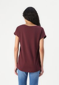 Top scurt de culoare burgundă, cu un fitting relaxat, decolteu rotund și manșete răsucite, asortat cu blugi din denim bleu deschis. Finisaj textil neted.