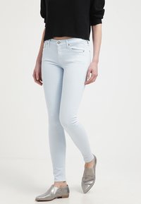 Jeans skinny de color azul claro hechos de denim, con un diseño ajustado y estilo clásico de cinco bolsillos, combinados con zapatos planos metálicos de color plateado.