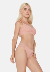 Ensemble lingerie rose clair comprenant un bralette sans couture avec des bretelles fines et une culotte assortie avec une accent en dentelle sur un côté.