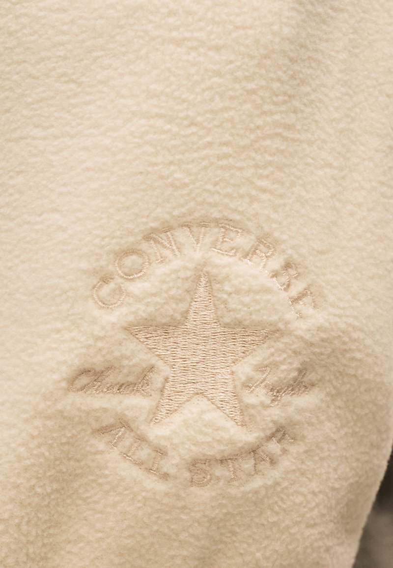 Embossed Converse All Star logo with a star in the center on beige textured fabric.