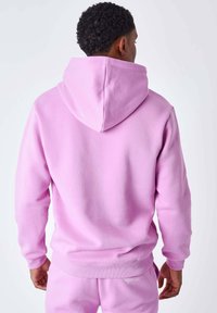 Sudadera con capucha de color rosa claro, fabricada con un material suave, que cuenta con una capucha grande y puños acanalados. Diseño sencillo sin logotipos ni estampados visibles.
