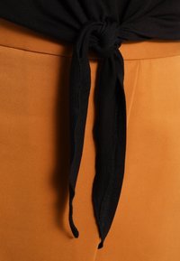 Tessuto nero annodato in vita di pantaloni color senape, mostrando una superficie liscia e un contrasto tra i due capi di abbigliamento.