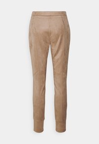 Pantalons en daim synthétique beige avec une coupe slim, présentant des jambes fuselées, une taille élastique et des coutures sur les côtés.