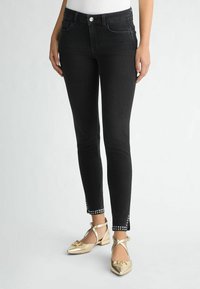 Jeans skinny in denim nero con una silhouette aderente, caratterizzati da dettagli decorativi con borchie all'orlo della caviglia e un classico design a cinque tasche.