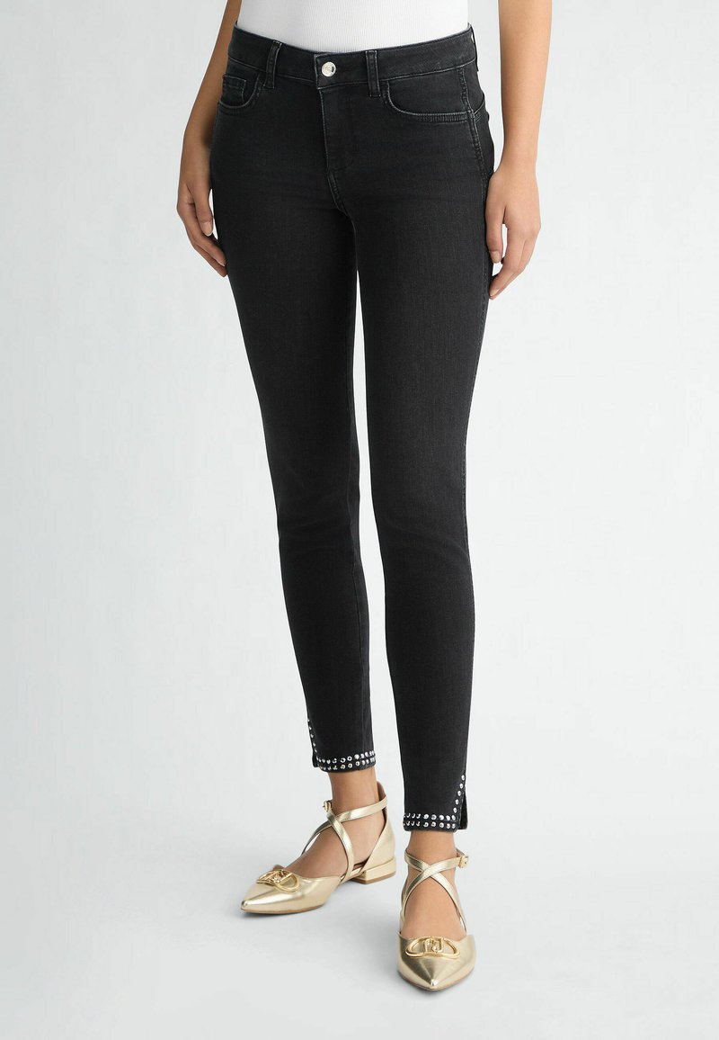 Jeans skinny in denim nero con una silhouette aderente, caratterizzati da dettagli decorativi con borchie all'orlo della caviglia e un classico design a cinque tasche.
