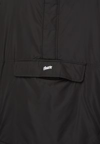 Jachetă neagră căptușită cu o textură netedă, o buzunar cu clapetă și un logo brodat pe spate. Design simplu și funcțional.