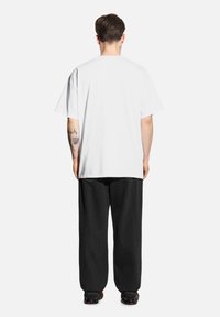 Biała bawełniana koszulka z krótkim rękawem, w połączeniu z luźnymi czarnymi spodniami. Spodnie mają lekko strukturalną powierzchnię i są noszone z czarnymi butami.