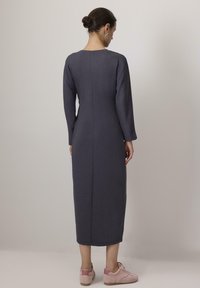 Vestido de manga larga, color gris oscuro, con una silueta ajustada, escote redondo y detalle de costura en la parte posterior. Combinado con zapatos casuales de color rosa claro.