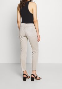 Ljust beige slim-fit jeans med bakfickor, i kombination med svarta klacksandaler. Toppen har en racerback-design i en solid svart färg.