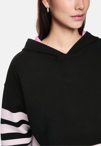 Black hoodie with a pink inner lining and striped sleeves in light pink and black. Soft fabric, featuring a classic hood and relaxed fit.