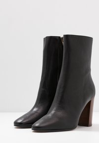 Black leather ankle boots with a smooth texture, pointed toe, and a chunky wooden heel. Features a side zipper for easy wear.