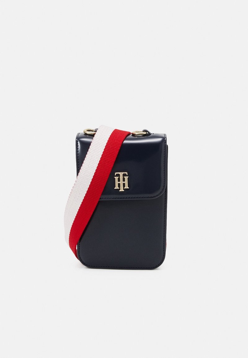 Navy blue crossbody bag made of glossy material, featuring a flap closure, gold logo hardware, and a striped red and white strap.