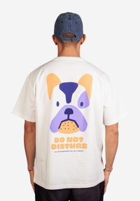 Weißes Baumwoll-T-Shirt mit einem bunten Cartoon-Hund auf dem Rücken und dem auffälligen Text "BITTE NICHT STÖREN" in Orange. Kurzärmelig, lockere Passform.