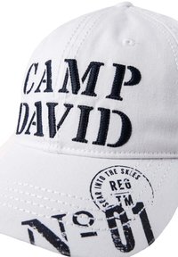White baseball cap featuring blue embroidered text "CAMP DAVID" and a circular graphic with "REG TM NO-01." Cotton fabric with visible stitching.