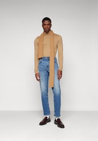 Beige ribbet langermet topp, lyseblå rette jeans, tan skjerf drapert, og mørk burgunder loafers med en glatt overflate.