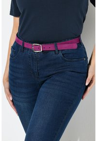Paarse suède riem met een zilveren metalen gesp, gedragen over donkerdenim jeans met een klassiek vijf-pocket ontwerp en een licht vervaagde textuur.