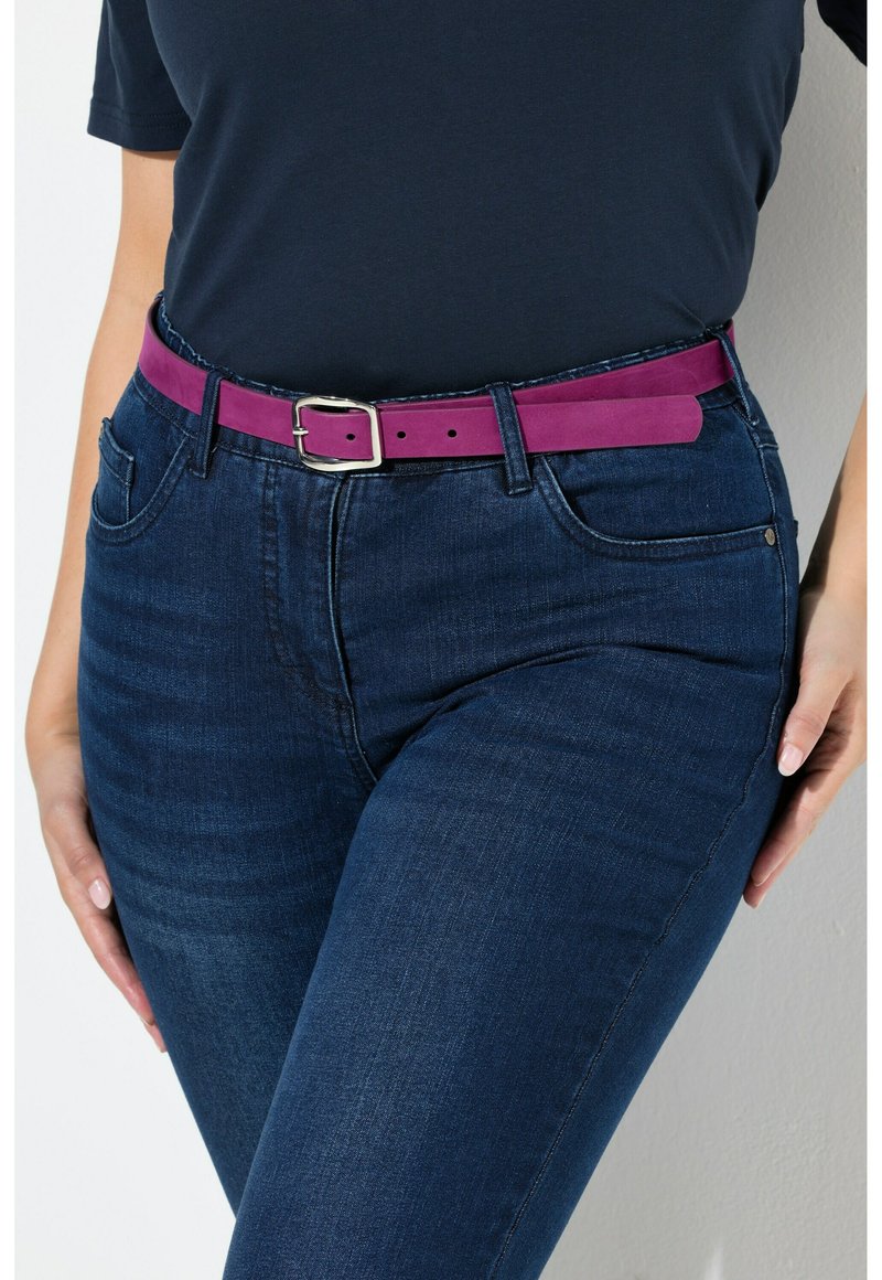 Paarse suède riem met een zilveren metalen gesp, gedragen over donkerdenim jeans met een klassiek vijf-pocket ontwerp en een licht vervaagde textuur.