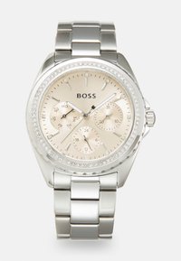 Montre en acier inoxydable argenté avec un boîtier rond, un cadran beige, des accents en cristal autour de la lunette et trois sous-cadrans.