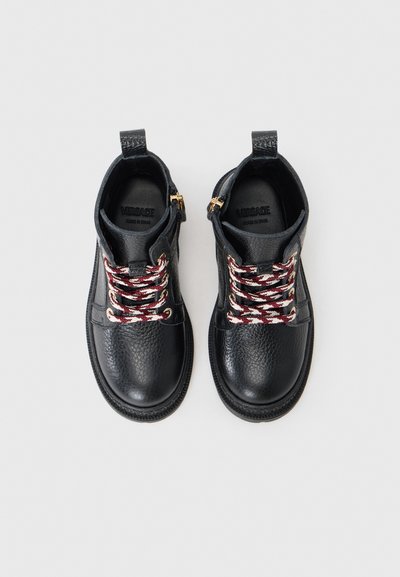 Svarta läderankelboots med en strukturerad yta, prydda med röda och vita flätade skosnören, guldfärgad hårdvara och dragflikar för enkel påtagning.