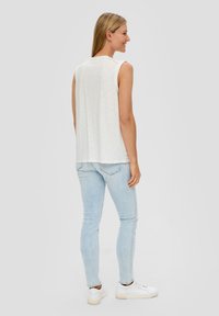 White sleeveless top with a relaxed fit, paired with light blue skinny jeans and white sneakers. Smooth texture and casual design.
