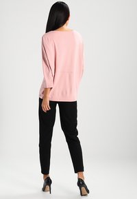 Haut rose clair, texturé, avec une coupe ample et des manches 3/4 associé à un pantalon noir ajusté et des talons noirs. Design simple sans motifs visibles.