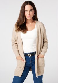 Beige lange cardigan gemaakt van zachte stof, met ribbels aan de mouwen, een open voorkant, twee voorzakken en een relaxed fit.