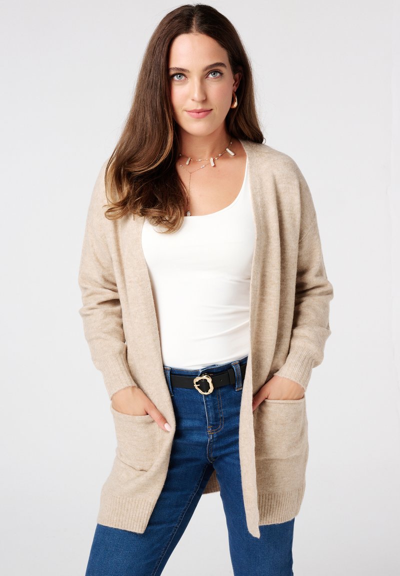 Beige lange cardigan gemaakt van zachte stof, met ribbels aan de mouwen, een open voorkant, twee voorzakken en een relaxed fit.