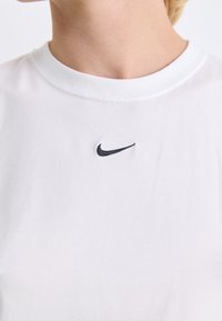 Balta trumpo rankovėmis marškinėliai, kurių priekyje, krūtinėje, yra juodai siuvinėtas Nike logotipas. Minkšta, glotni medžiaga su apvaliu kaklo išpjovu.