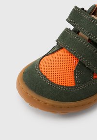 Πράσινη σουέτ δερμάτινη παπούτσι με πορτοκαλί πλέγμα πάνελ, διαθέτει δύο ρυθμιζόμενους ιμάντες με βέλκρο και καφέ λαστιχένια σόλα. Κοντινή άποψη που αναδεικνύει την υφή.