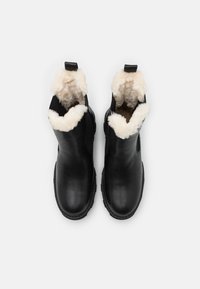 Bottines en cuir noir avec une doublure en fourrure crème, dotées d'une tirette et de panneaux latéraux élastiques, avec des semelles en caoutchouc texturé.
