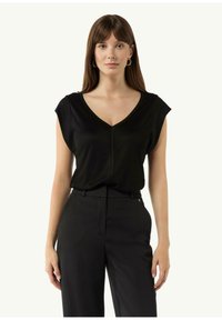 Schwarzes V-Ausschnitt-Oberteil mit kurzen Ärmeln, strukturiertem Stoff und einer mittigen Naht. Kombiniert mit schwarzen, taillierten Hosen. Minimalistisches Design.