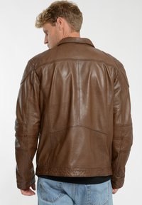 Brun läderjacka med texturerad yta, synliga stygn och platt krage, som har en avslappnad passform och klassisk design.