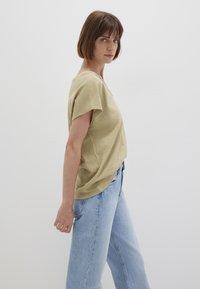 Olive green linen blend top with a loose silhouette, short sleeves, and a wide neckline, paired with light blue high-waisted jeans.