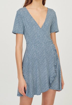 Robe portefeuille florale bleue avec des manches courtes, décolleté en V, détail volanté sur le côté, faite en tissu léger, avec un motif blanc éparpillé.