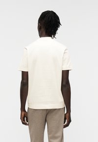 Κρεμ κοντομάνικο μπλουζάκι με ίσια γραμμή  και στρογγυλή λαιμόκοψη, κατασκευασμένο από απαλό ύφασμα, συνδυασμένο με ανοιχτό γκρι casual παντελόνια.