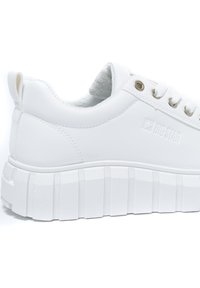 Bílé tenisky na platformě s tlustou, vroubkovanou podrážkou, hladkým syntetickým svrškem, kovovými průchody na tkaničky a logem vyraženým na boku.