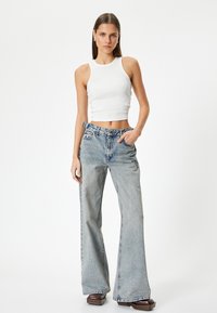 Valkoinen ribattu crop-top, joka on yhdistetty vaaleansinisiin leveälahkeisiin farkkuihin. Farkuissa on korkea vyötärö, hienovarainen haalistuminen ja klassinen viisi taskua -design.
