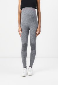 Leggings grigio a vita alta con una texture melange, caratterizzati da accenti rosa sul elastico in vita e sulle toppe delle ginocchia, abbinati a sneakers bianche.