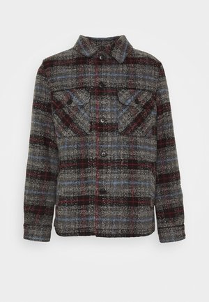 Veste en laine boutonnée avec motif à carreaux gris, noir, rouge et bleu, deux poches poitrine à rabat et un col droit, vue de face.