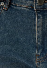 Tejido de denim azul oscuro, con costuras naranjas, un botón de metal y una ligera textura con patrones de tejido visibles y una caída suave.