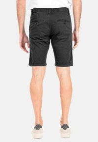 Shorts neri in cotone con taglio dritto, tasche posteriori con patte abbottonate e orlo pulito. Indossati con sneaker casual.