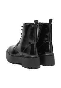 Czarne lakierowane buty wojskowe na grubej platformie, z przodem sznurowanym i zamkiem błyskawicznym z boku. Charakteryzują się gładkim, błyszczącym wykończeniem.