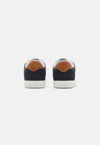 Navy sneakers with a textured fabric upper, tan suede heel accents, grey interior lining, and white rubber soles.